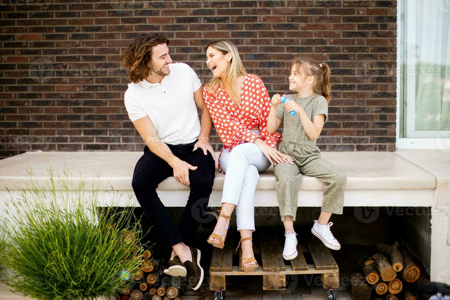 Family with a mother, father and daughter sitting outside on the steps of a front porch of a brick house photo