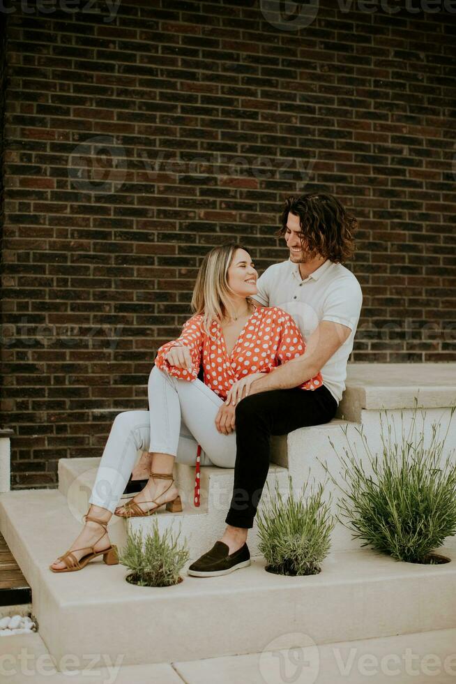 Smiling young couple in love sitting in front of house brick wall photo