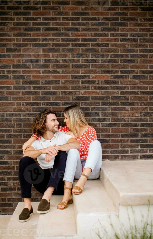 Smiling young couple in love sitting in front of house brick wall photo