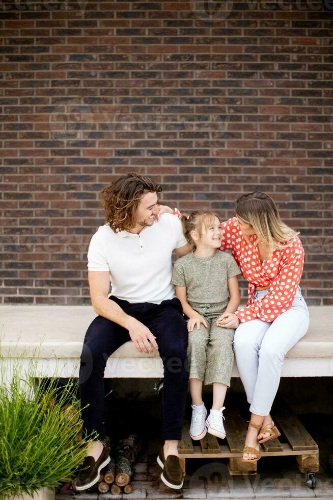 Family with a mother, father and daughter sitting outside on the steps of a front porch of a brick house photo