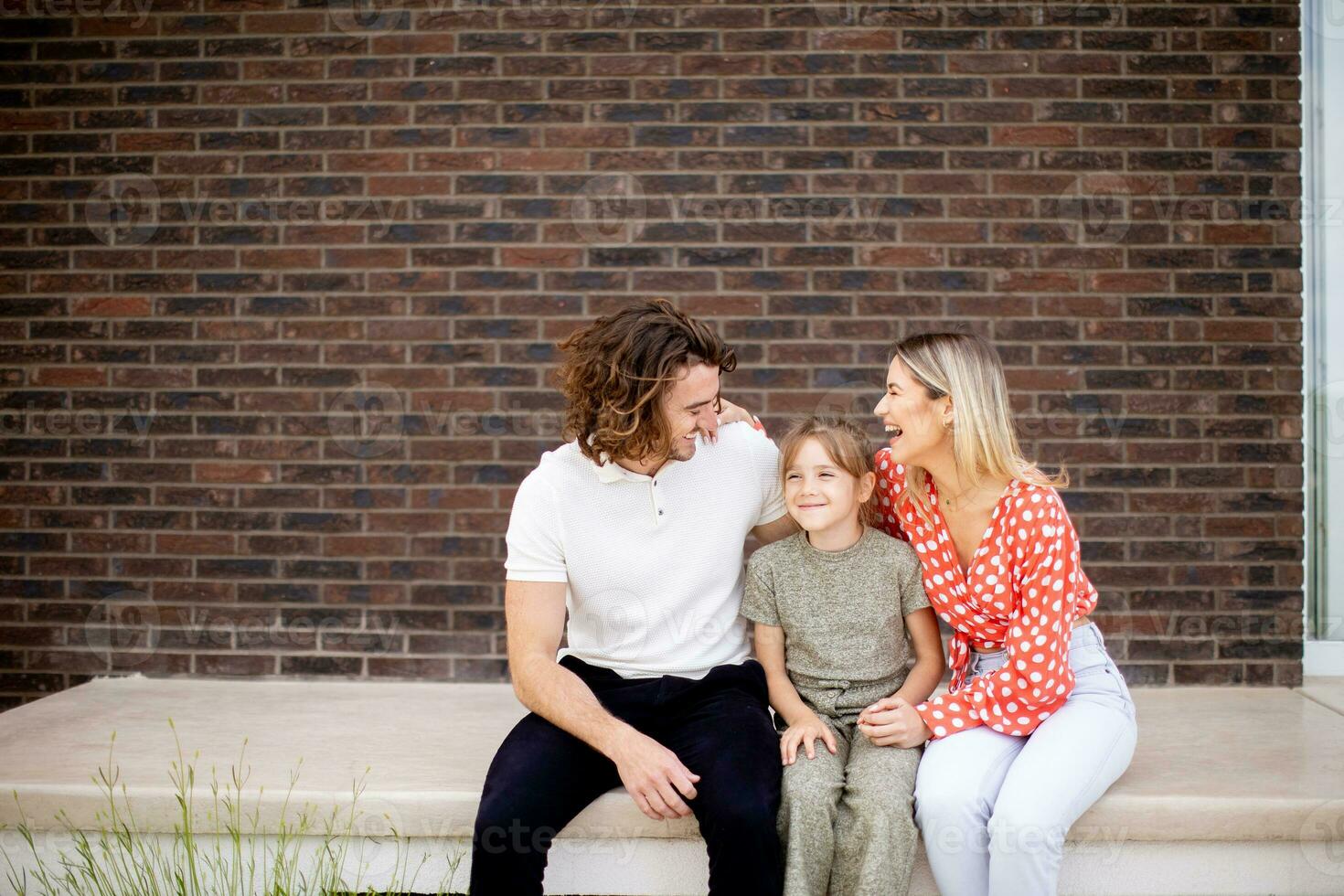 Family with a mother, father and daughter sitting outside on the steps of a front porch of a brick house photo