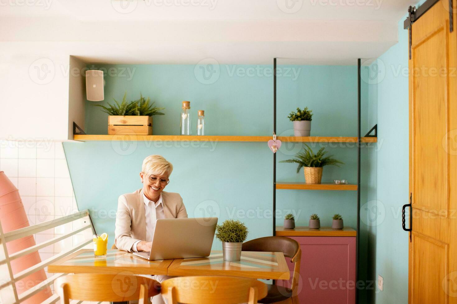 Senior woman using mobile phone while working on laptop and drinking fresh orange juice in the cafe photo