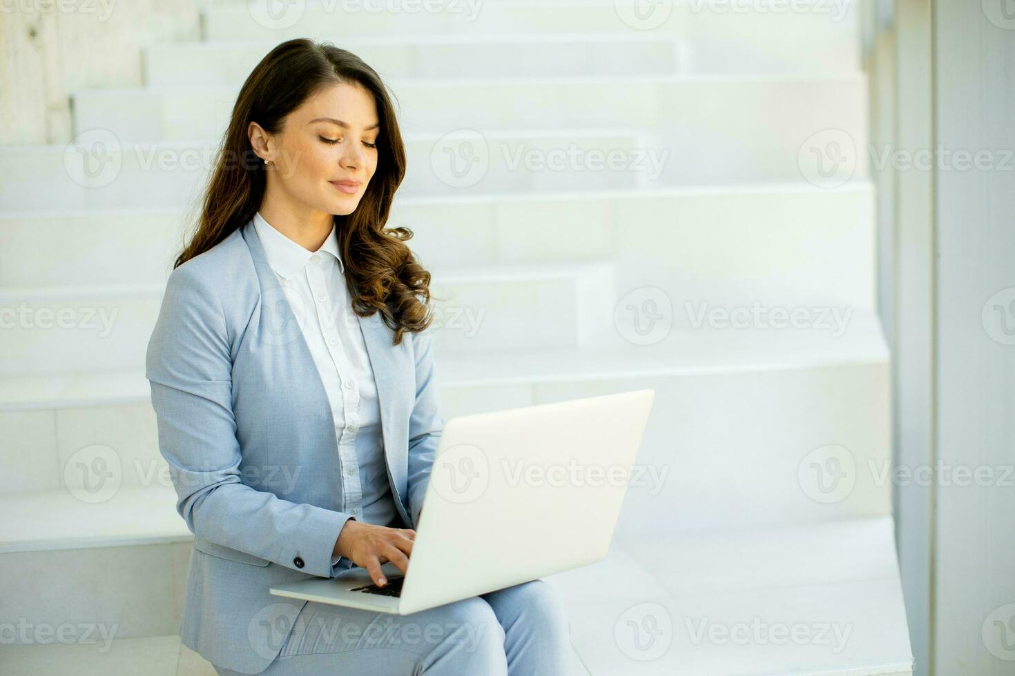 Young business woman sitting on the stairs on office hallway and working on laptop photo