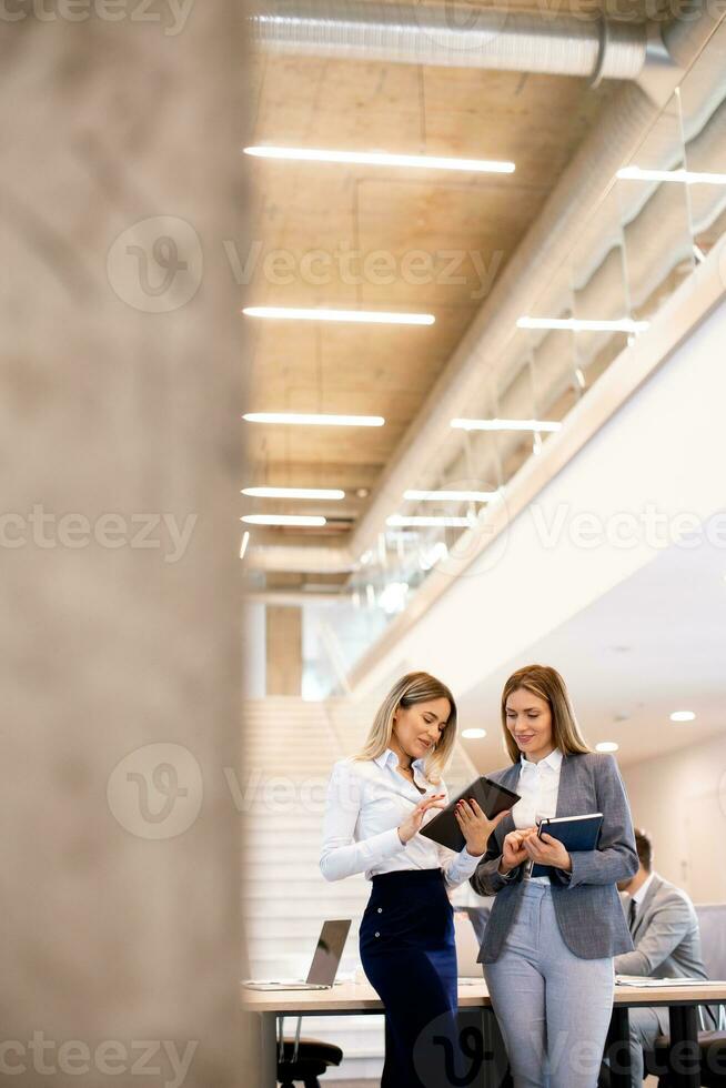 Two young business women looking at financial results on digital tablet in front of their team at the office photo