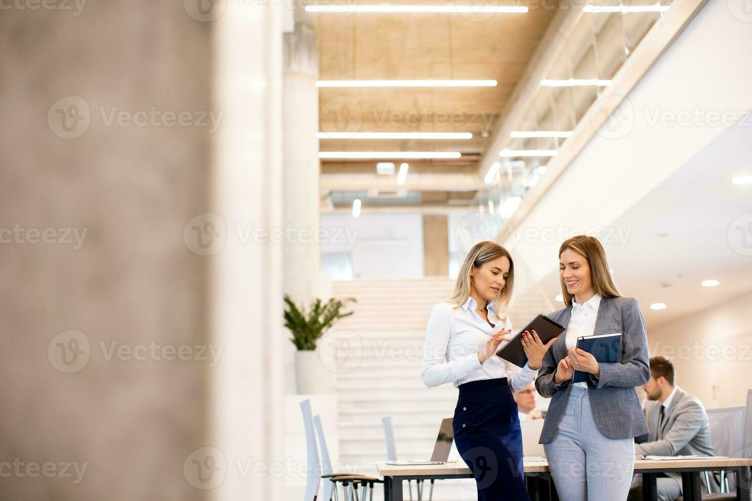 Two young business women looking at financial results on digital tablet in front of their team at the office photo