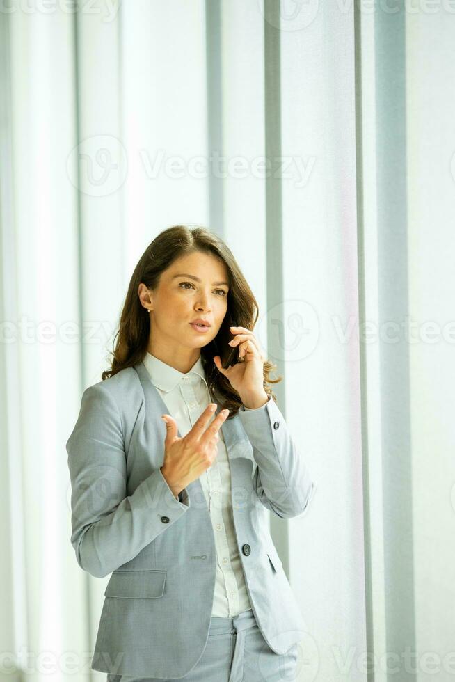 Young woman using mobile phone by the office window photo