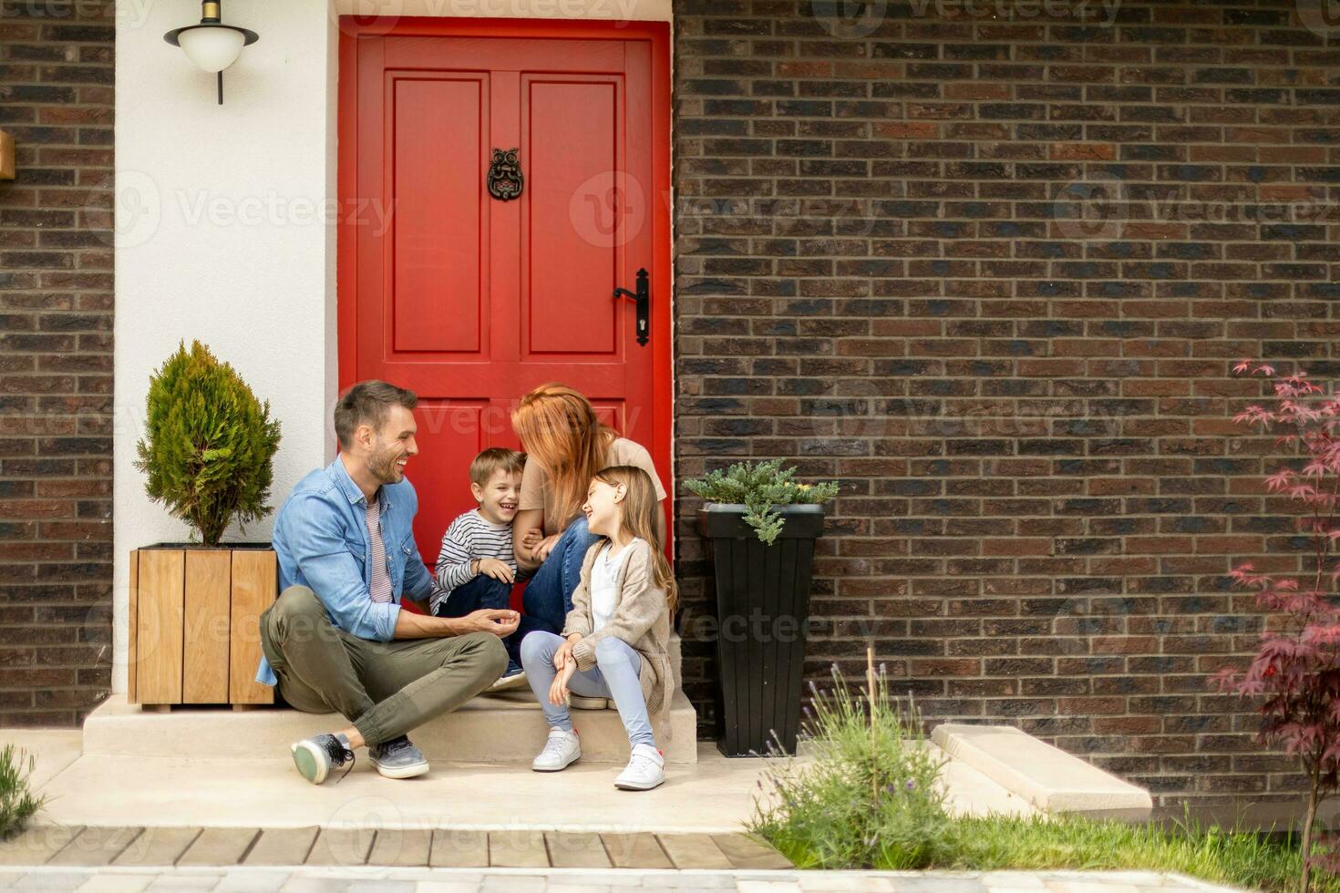 Family with a mother, father, son and daughter sitting outside on the steps of a front porch of a brick house photo