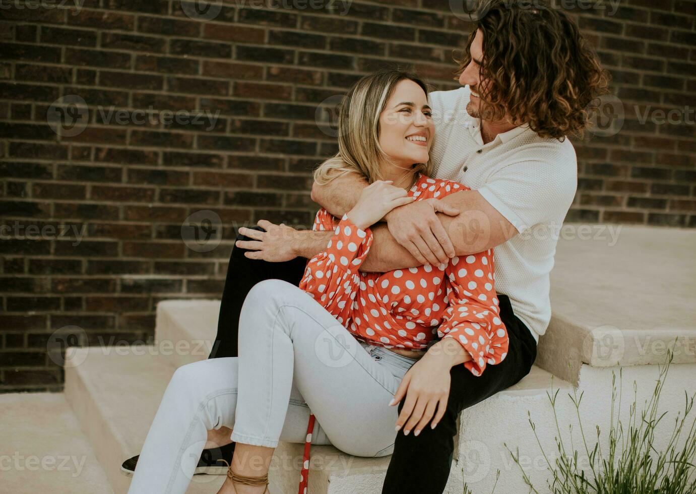 Smiling young couple in love sitting in front of house brick wall photo