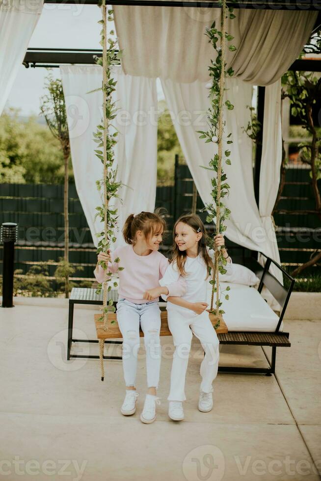 Cute little girls on the swing in the house backyard photo