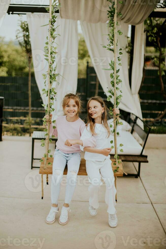 linda pequeño muchachas en el columpio en el casa patio interior foto