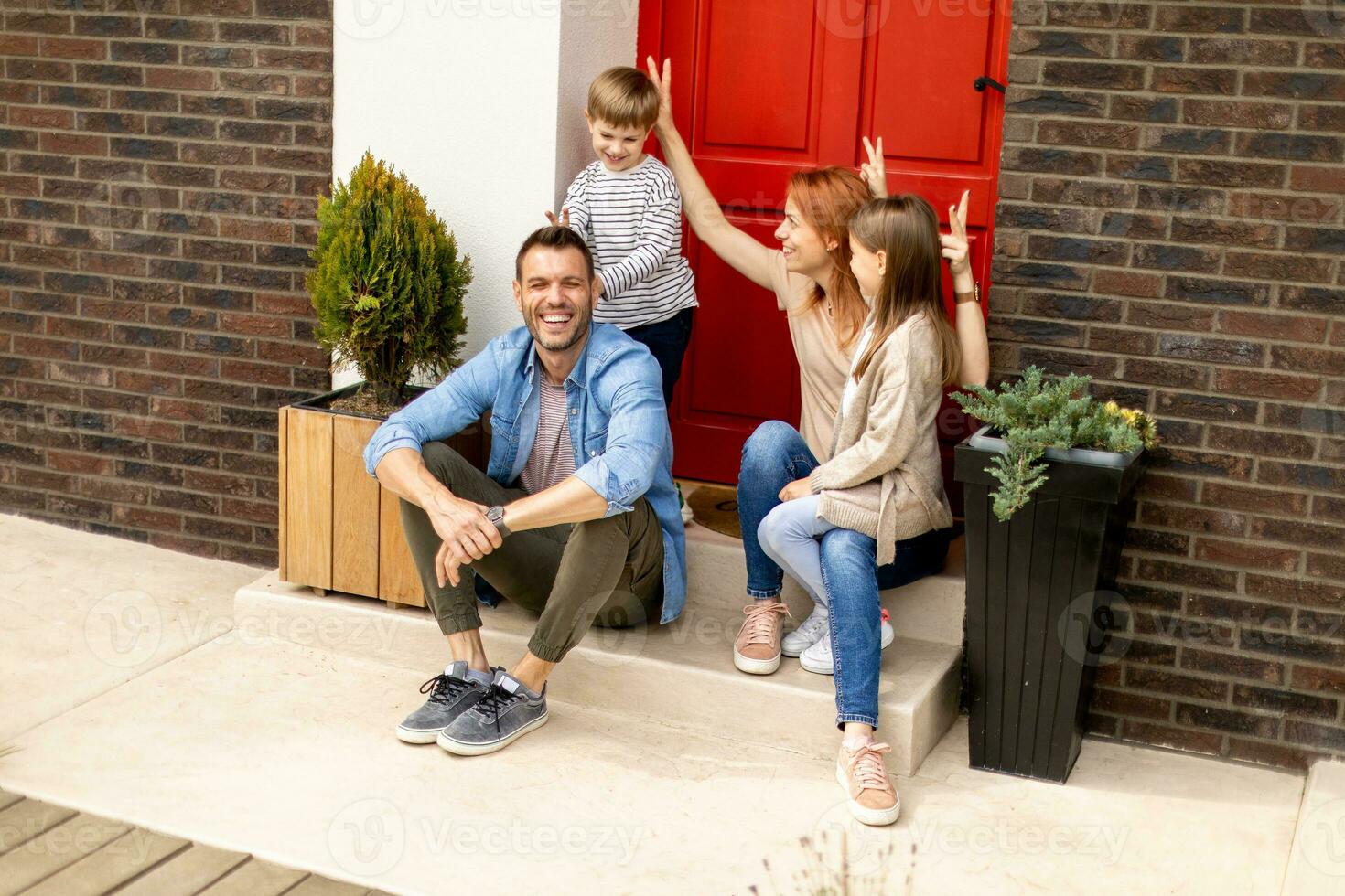 Family with a mother, father, son and daughter sitting outside on the steps of a front porch of a brick house photo