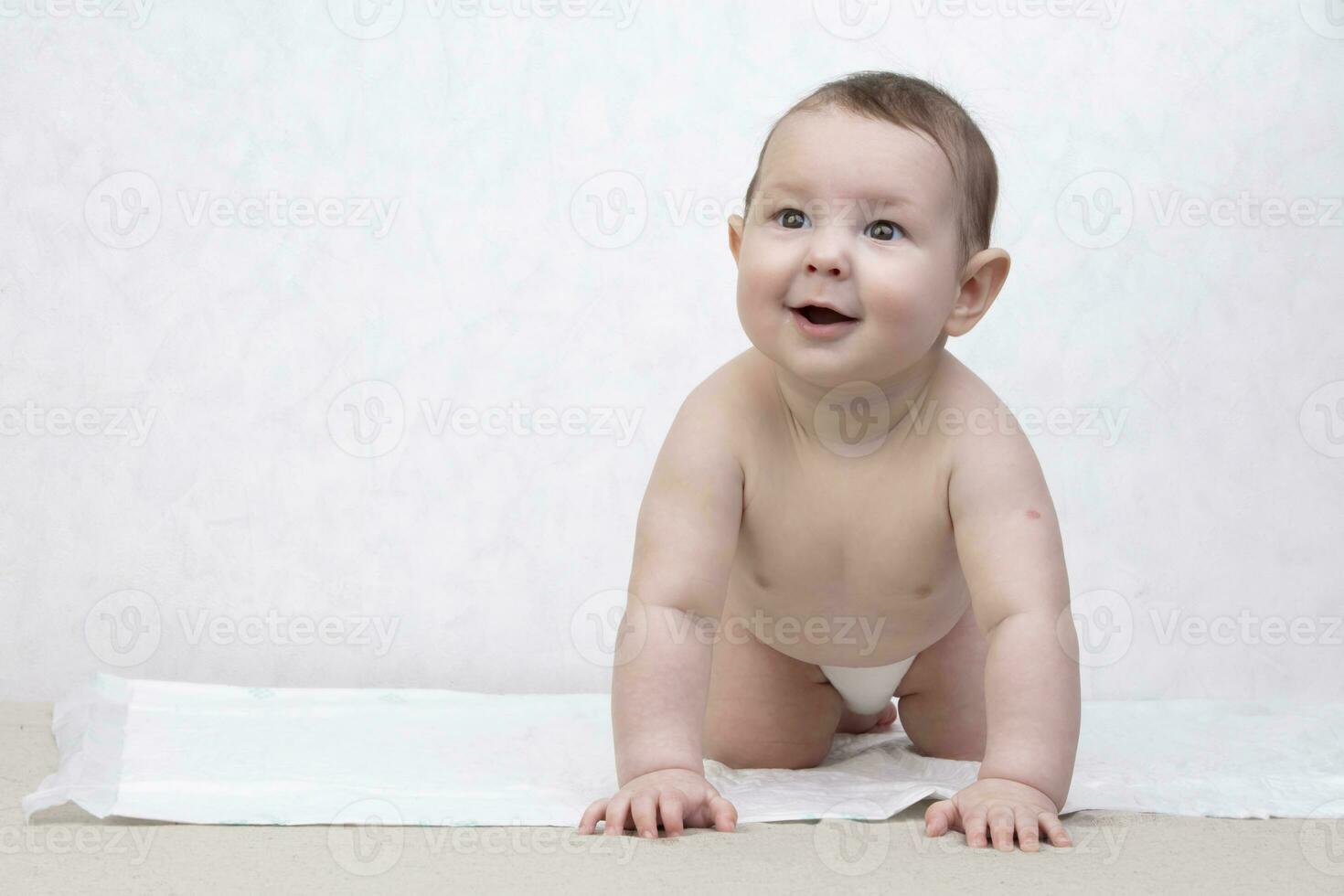 Kid with a smile on a white background. A happy six month old boy crawls on the bed and laughs. Conceptual photo of fatherhood and motherhood.