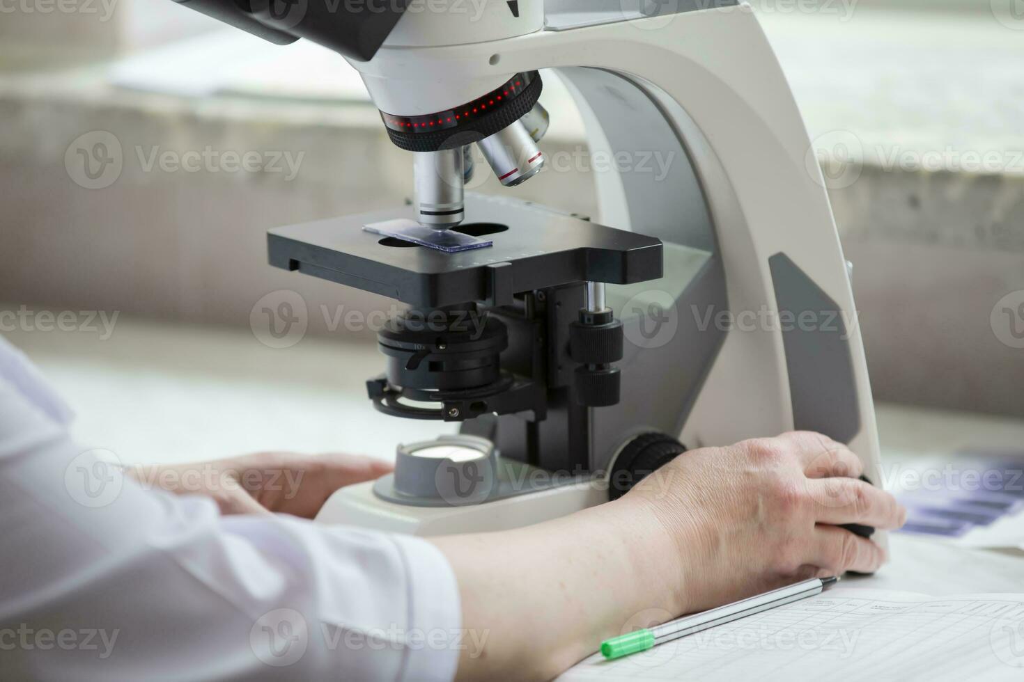 Part of a laboratory microscope in a hospital with the hands of a laboratory assistant. photo