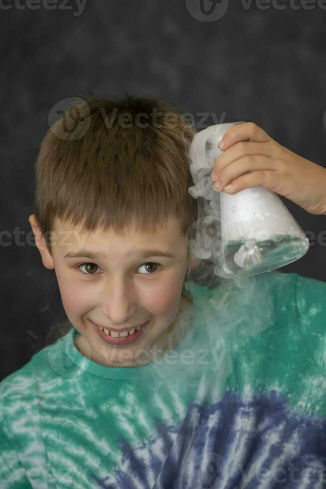 un chico conduce un científico químico experimentar con líquido nitrógeno. un niño con un vaso matraz lleno con fumar. foto