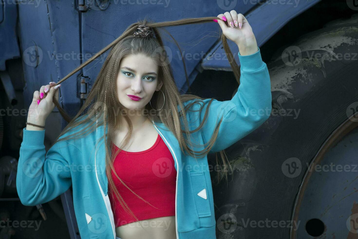 A beautiful country girl in the style of the 90s in bright clothes stands near a tractor. photo