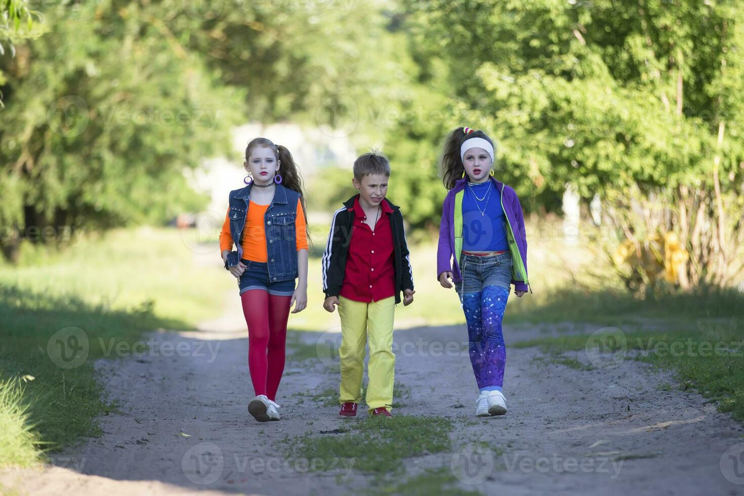 Cheerful kids a boy and two girls in cool outfits are walking along the road photo