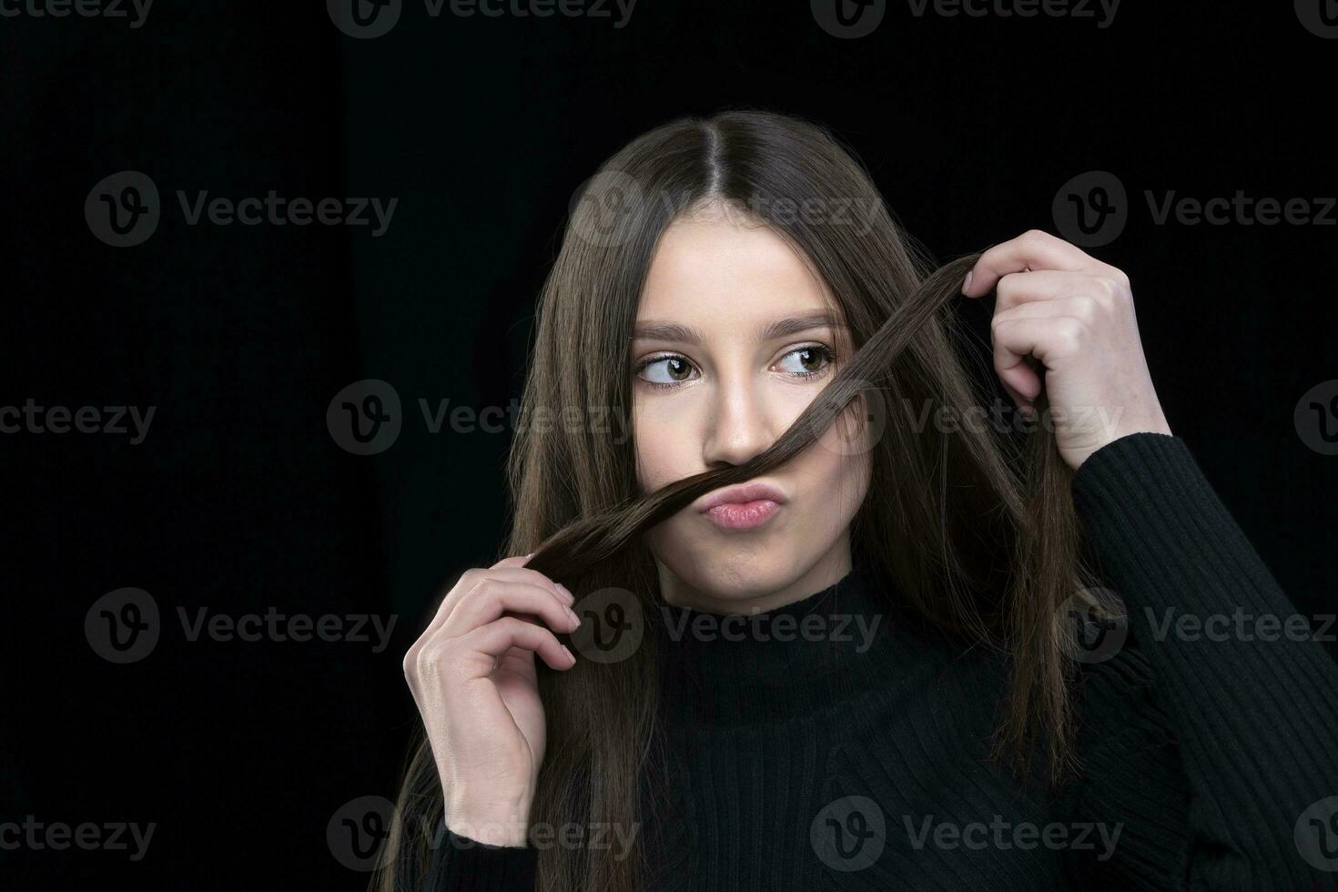 A beautiful girl with long hair fooling around in front of the camera. Makes a mustache out of hair. photo