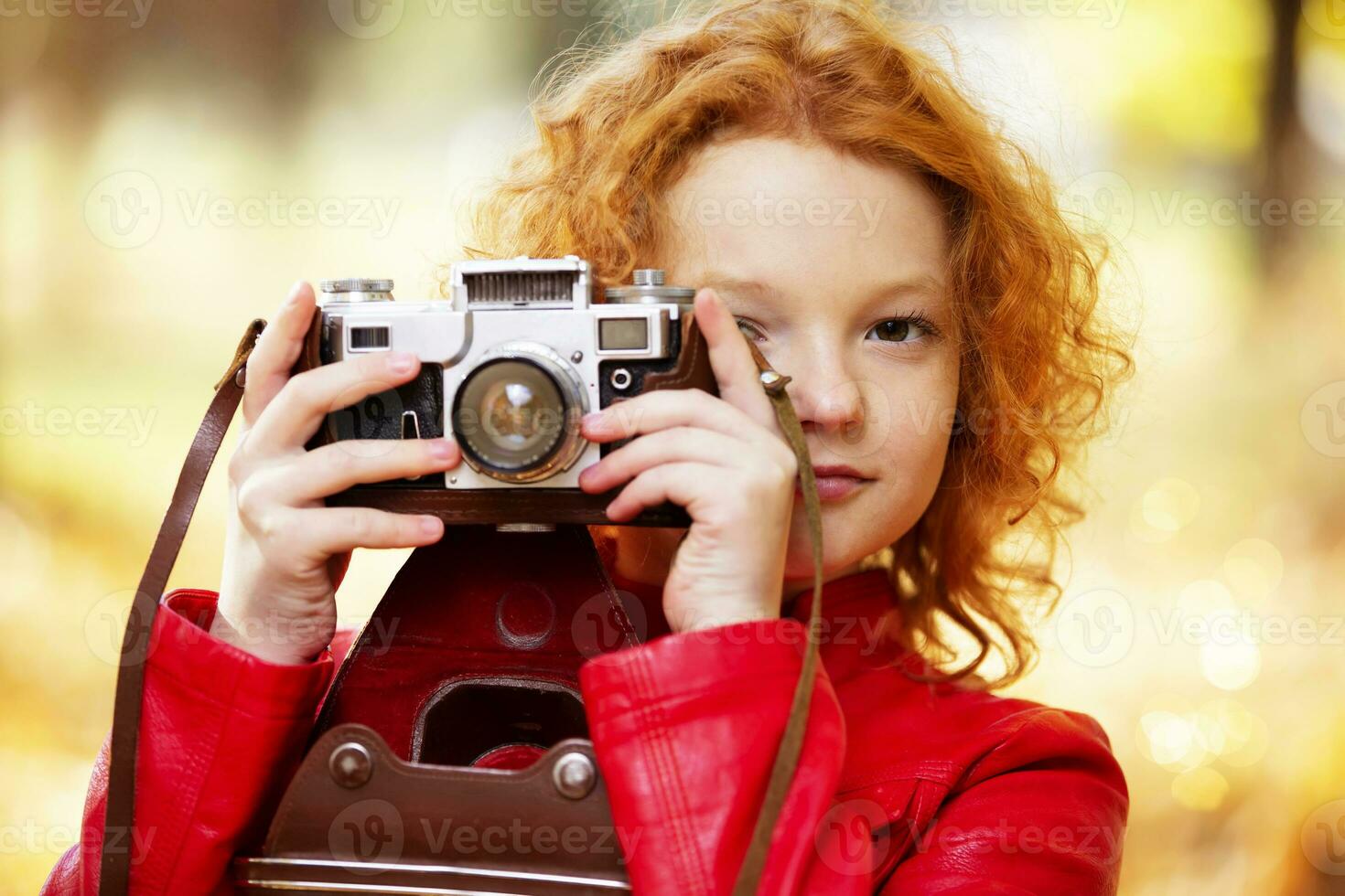 Little red-haired girl with a retro camera on an autumn background. photo