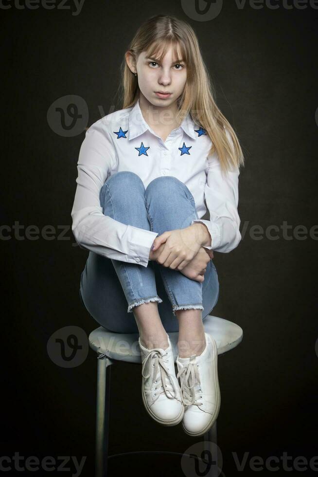 Beautiful teenage girl in jeans and a white shirt is shot against a gray background. photo