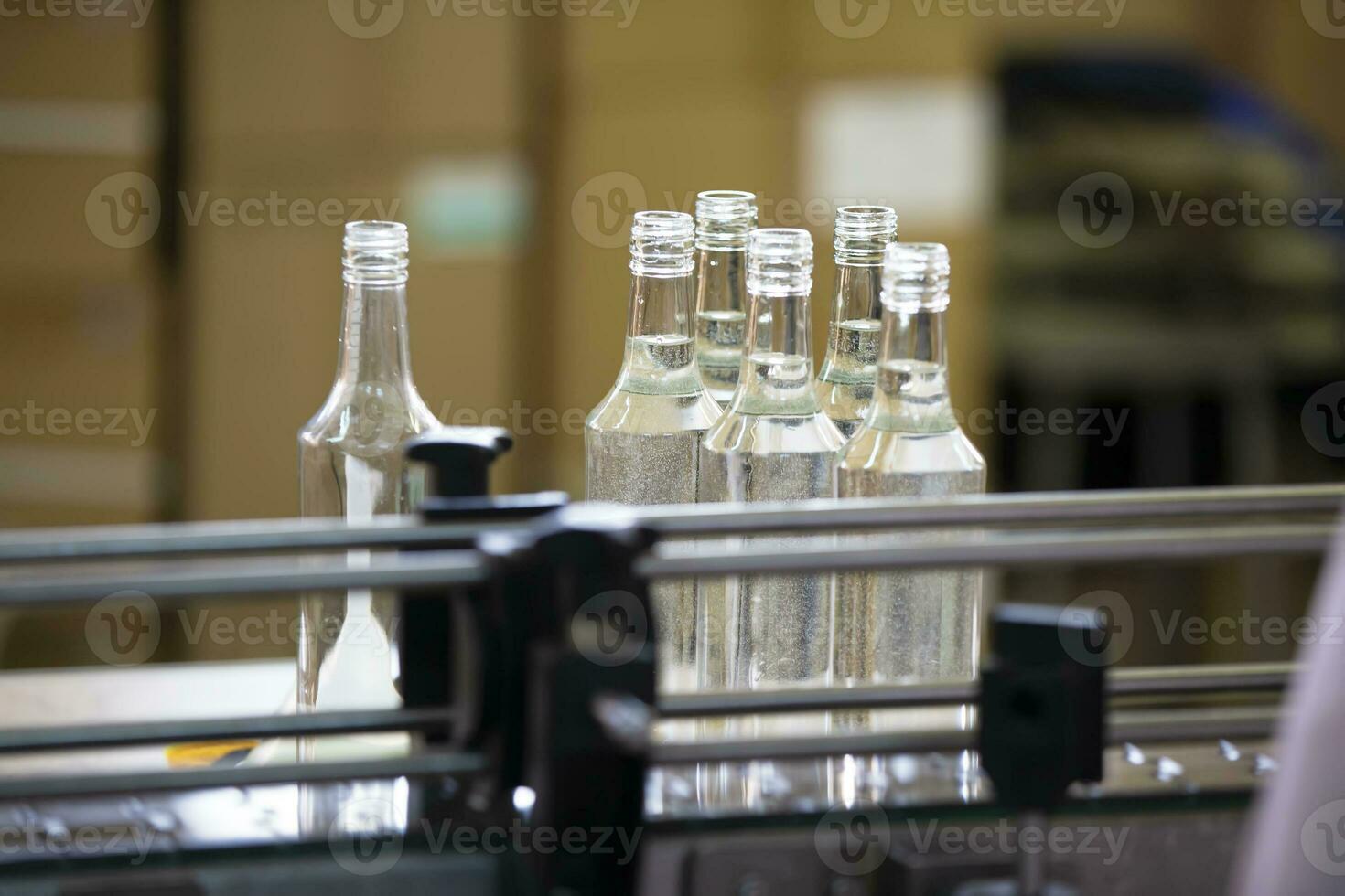 un fila de vaso botellas en un transportador cinturón para el producción de alcohólico bebidas foto