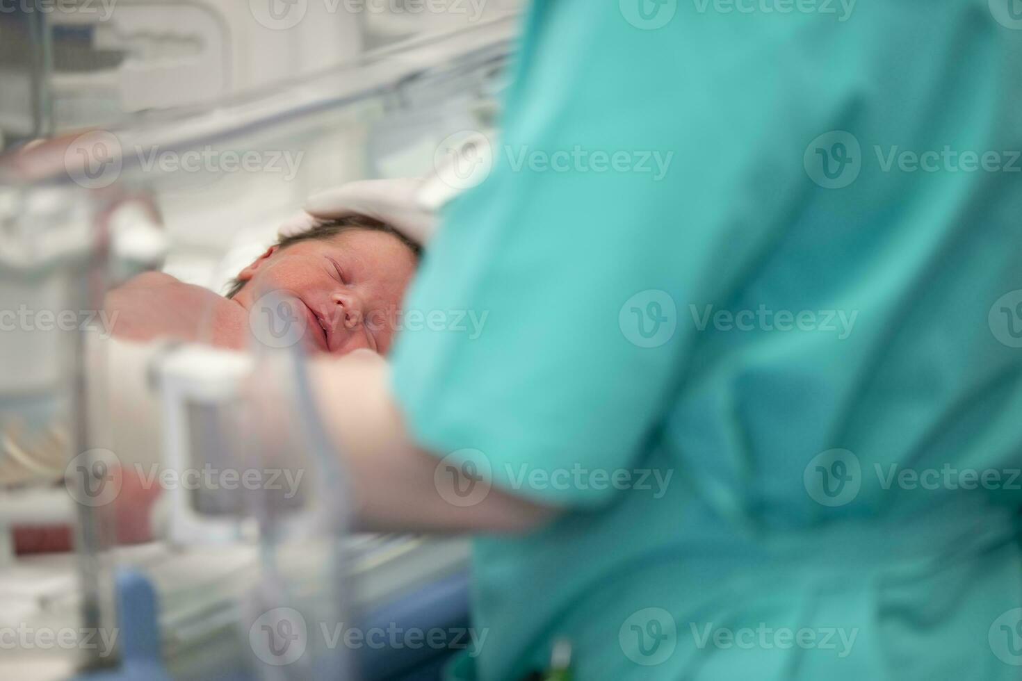 The doctor's hands in rubber gloves are holding the head of a newborn baby who lies in the medical box. photo