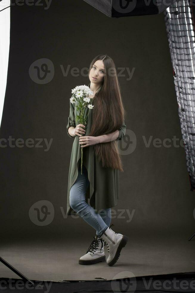 Beautiful brunette girl with very long hair under studio equipment in a photo studio. Woman fashion model posing at the camera.