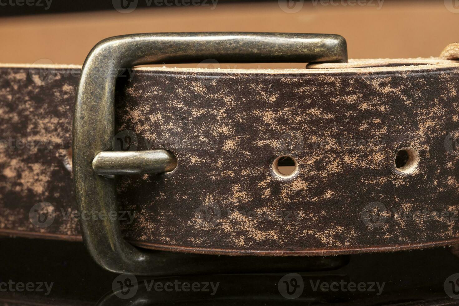 Brown leather belt with scuffs and a metal buckle on a dark background. photo