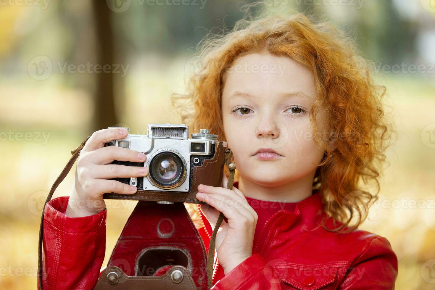 pequeño Pelirrojo niña con un retro cámara en un otoño fondo