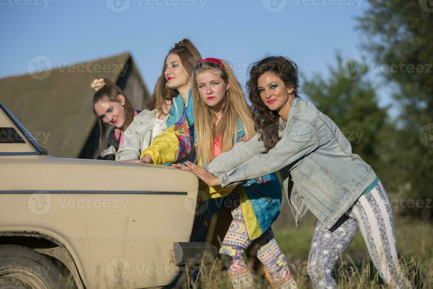 Young cheerful girls are pushing an old car. Women in the style of the 90s. photo