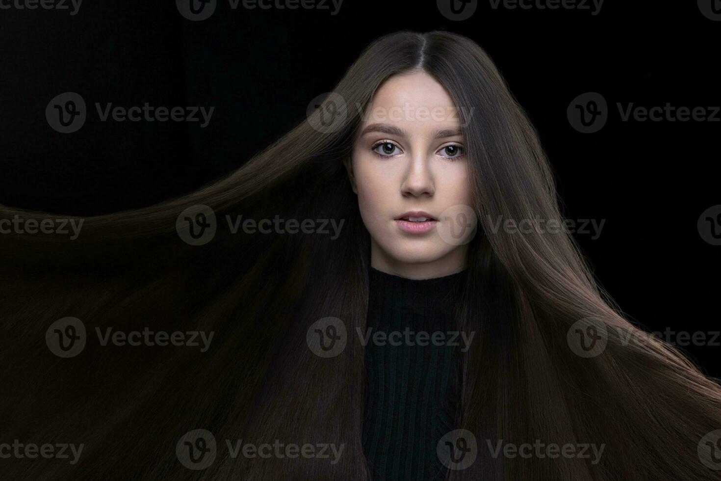 un hermosa joven niña con natural belleza con largo suave pelo en un oscuro antecedentes. foto