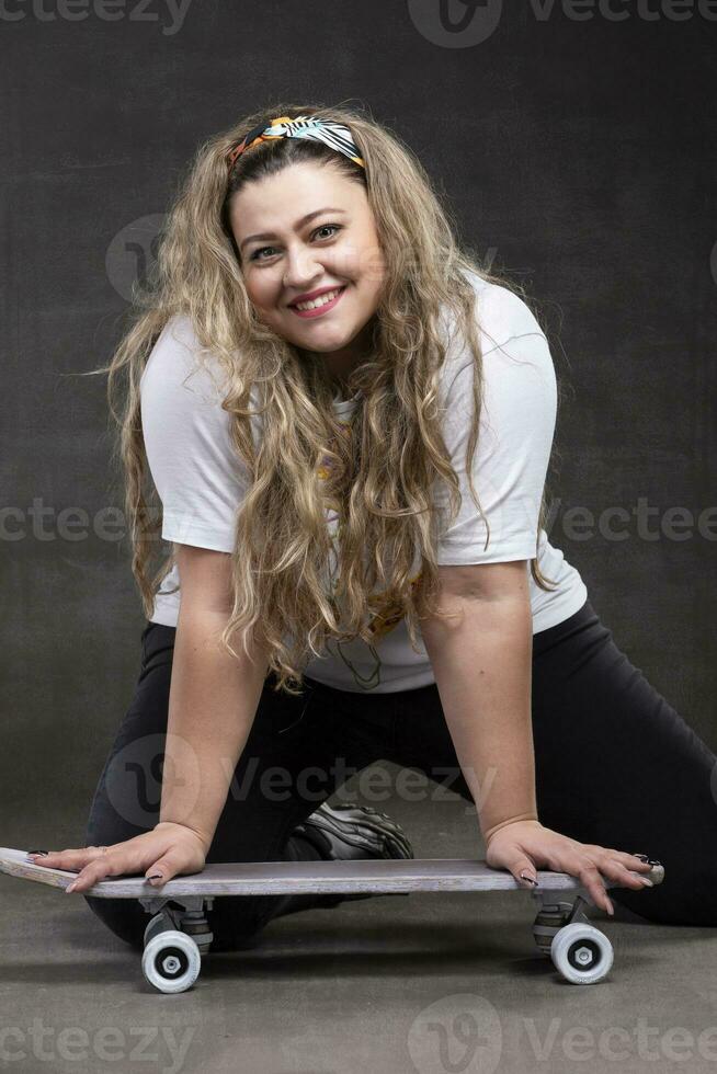 hermosa grasa mujer con un patineta en un gris antecedentes mira a el cámara y sonrisas foto