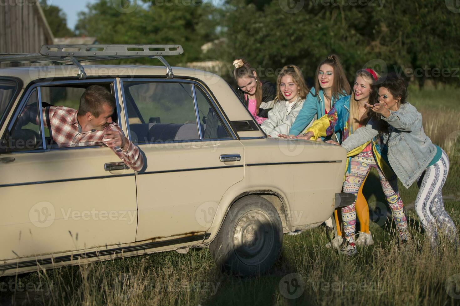 Young cheerful girls are pushing an old car. Women in the style of the 90s. photo