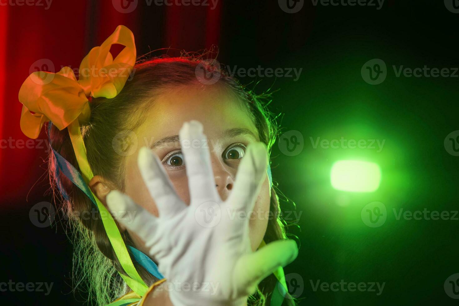 el pequeño Actriz niña cubierto su cara con un blanco guante y mira mediante su dedos. etapa ligero y niño actor. foto