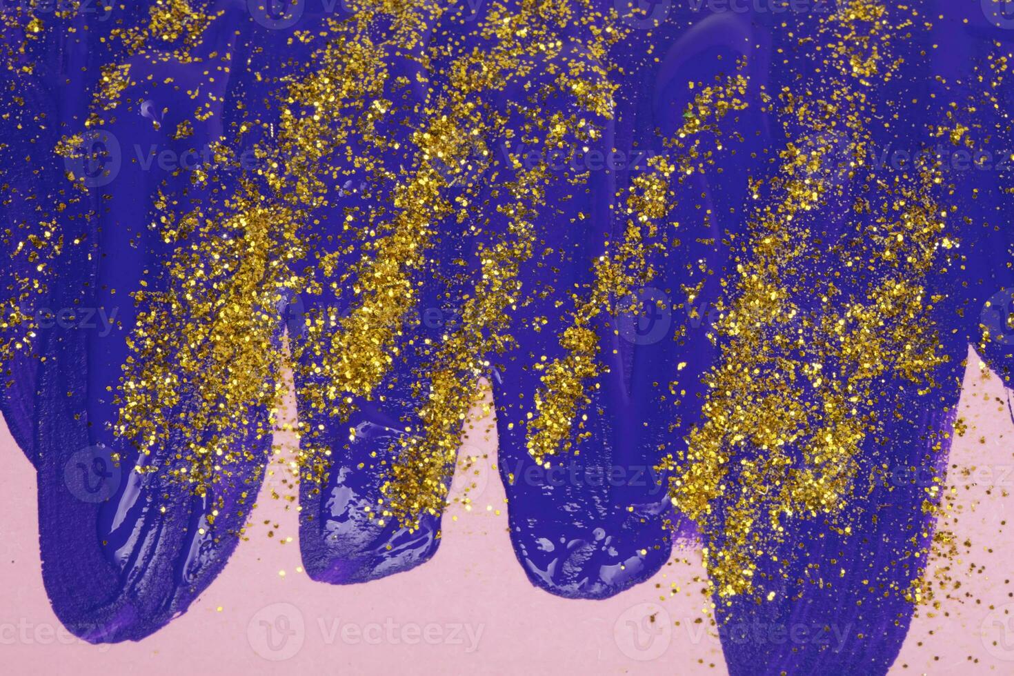 On a pink background, blue iridescent smudges of flowing acrylic paint with gold sparkles. photo