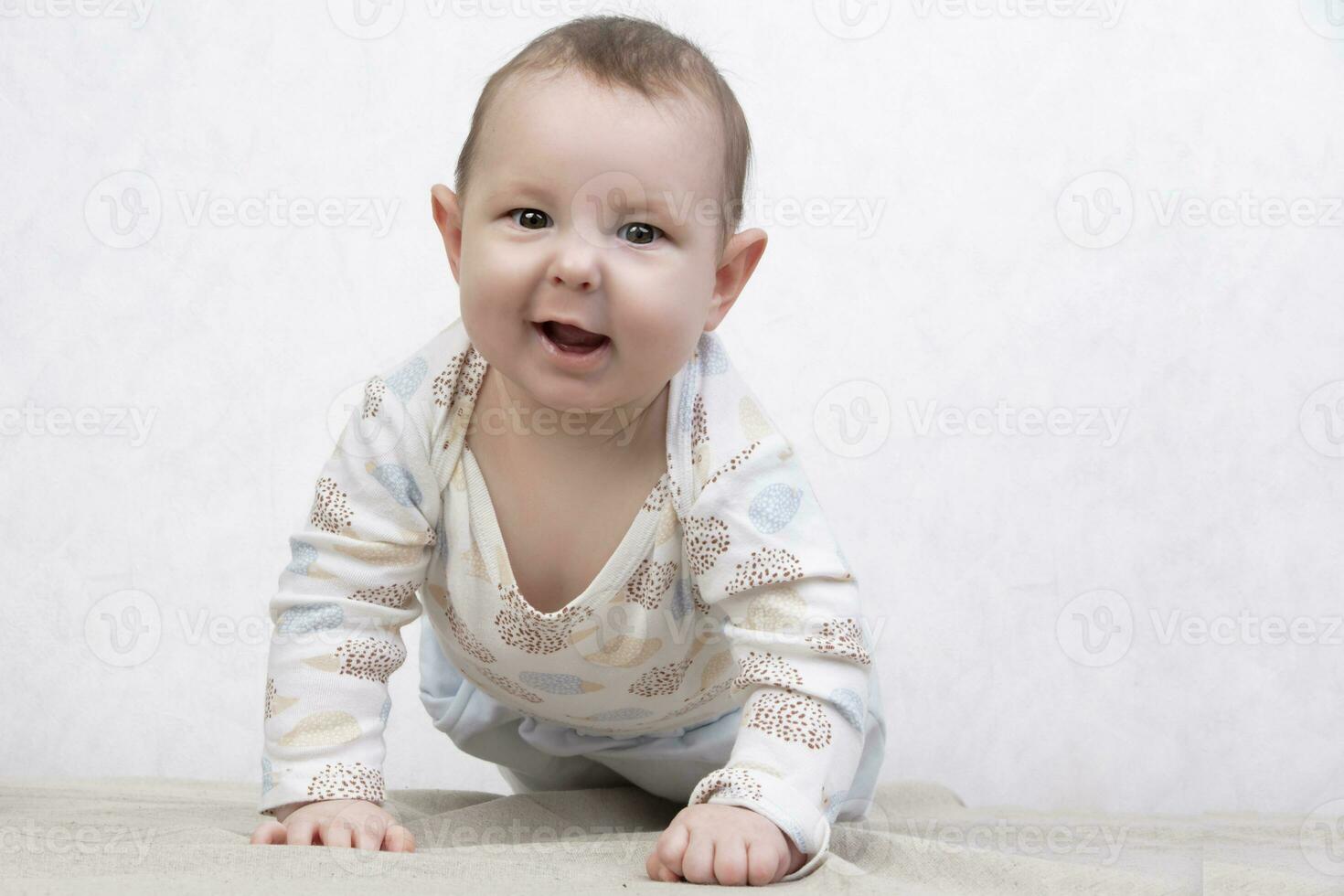 Kid with a smile on a white background. An adorable six month old baby crawls on the bed. Conceptual photo of fatherhood and motherhood.