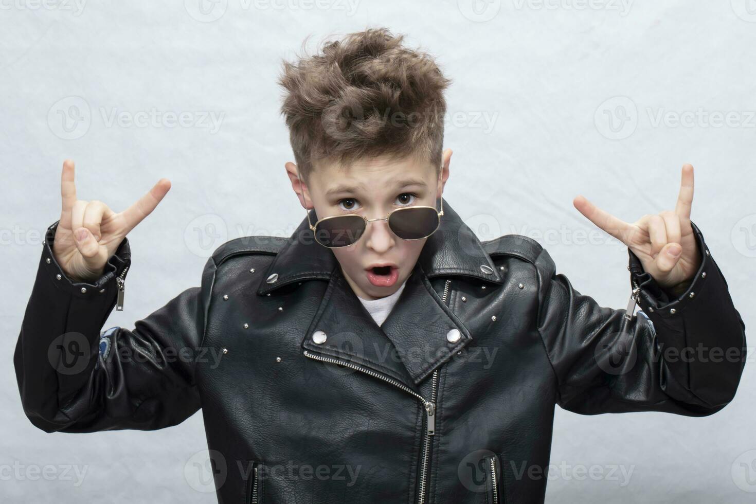 Portrait of a heavy metal boy in sunglasses. Cute teenager in a leather jacket doing a rock and roll sign photo