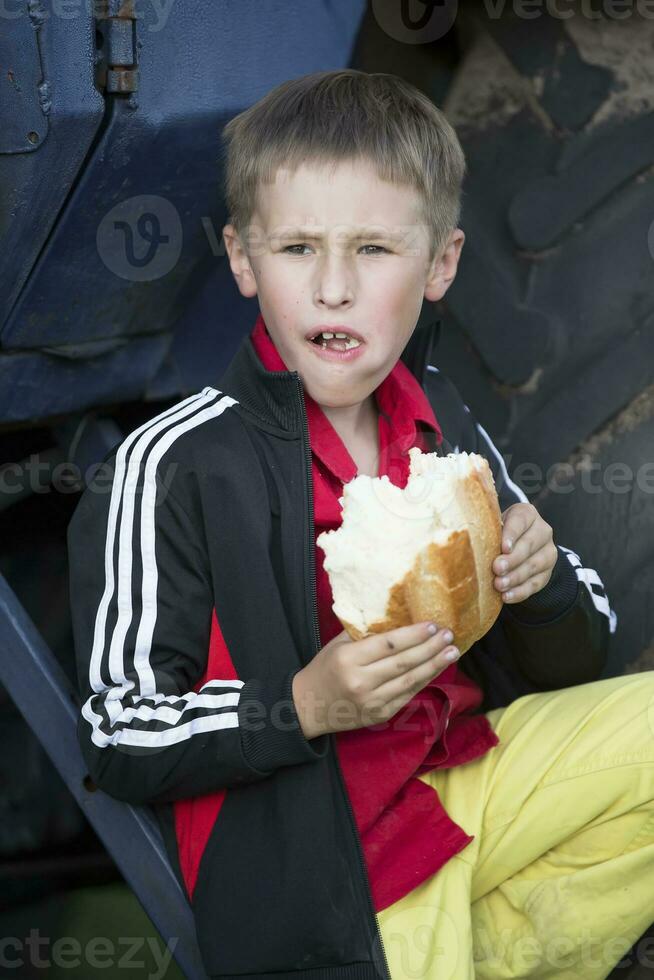 un gracioso pequeño chico es hambriento y es comiendo un grande bollo. foto