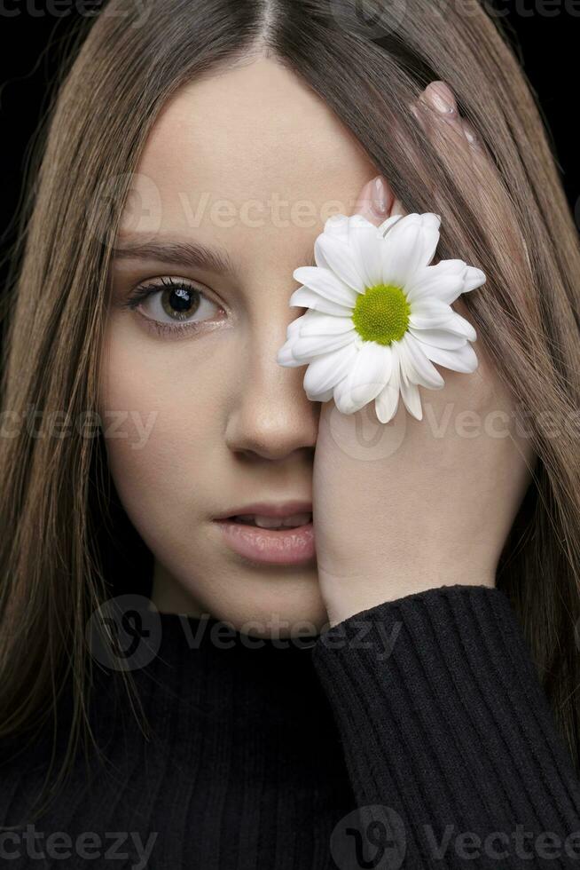 A beautiful girl with natural beauty holds a white flower near her eye. Young girl with a white chrysanthemum. photo