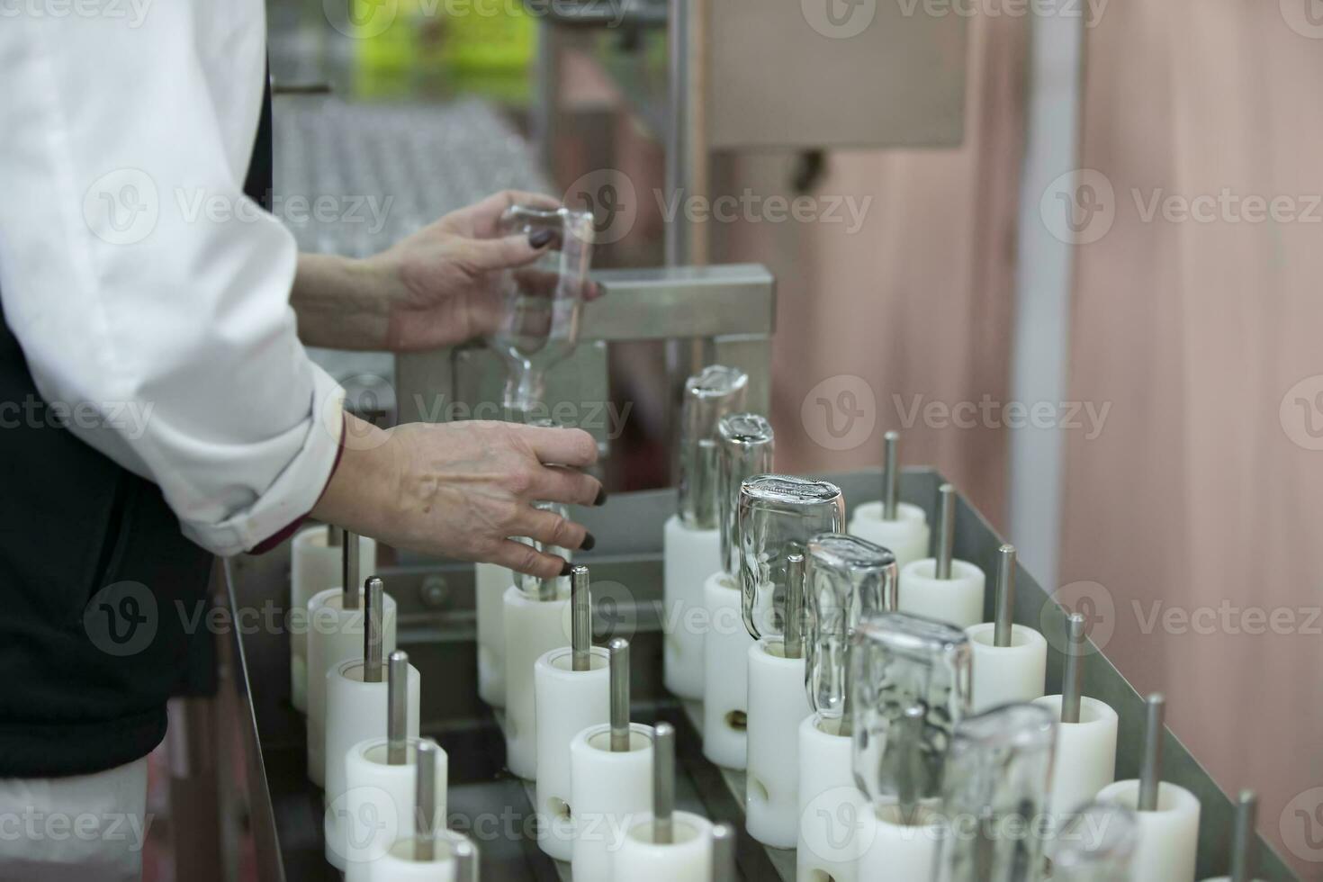 un fila de vaso botellas en un transportador cinturón para el producción de alcohólico bebidas foto