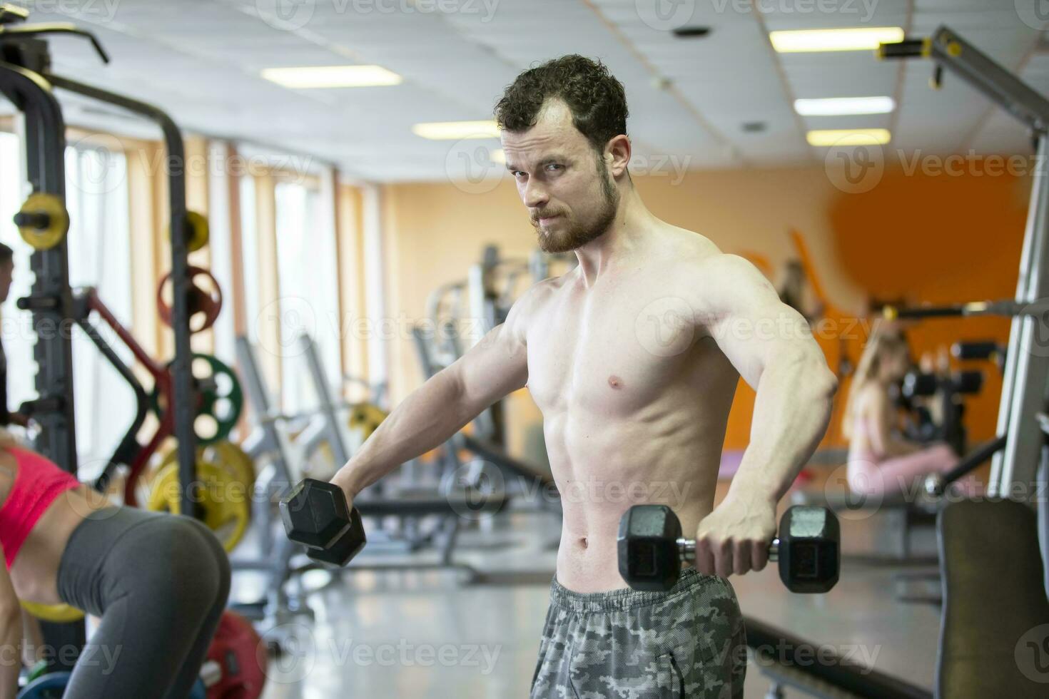 un joven hombre de atlético físico es comprometido con pesas en el gimnasia. foto