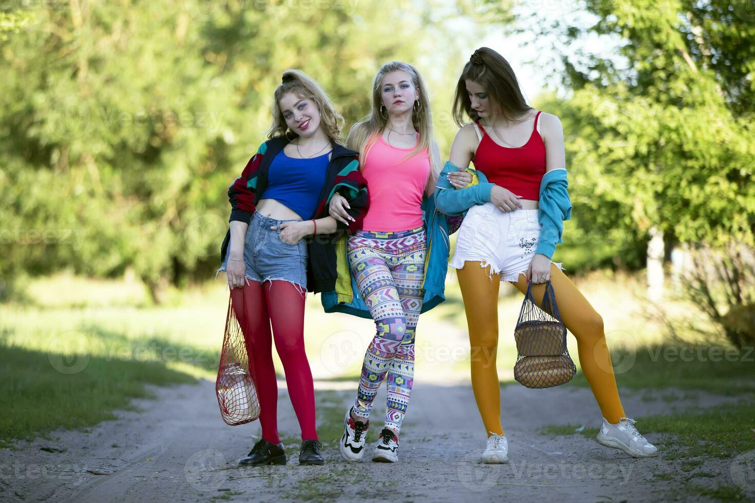 Three beautiful country girls dressed in the style of the nineties are walking along the road. photo