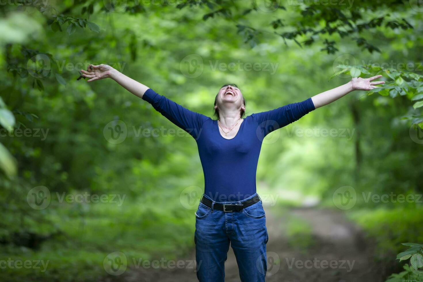 Happy middle-aged woman spread her arms in the forest. photo