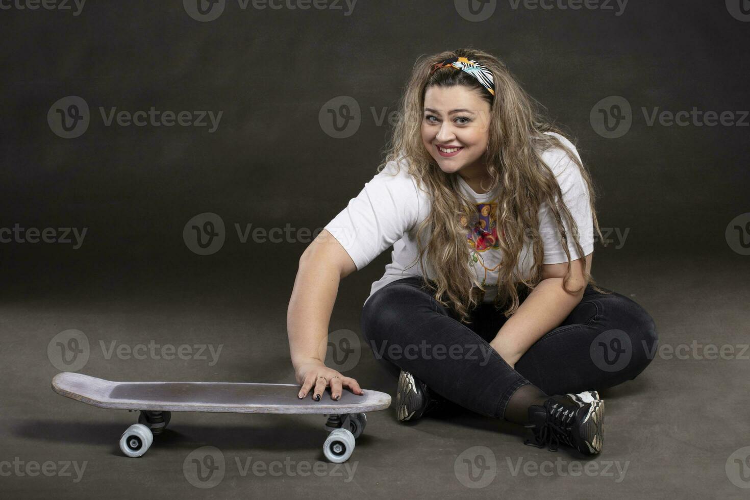 hermosa rechoncho mujer con un patineta en un gris antecedentes. foto