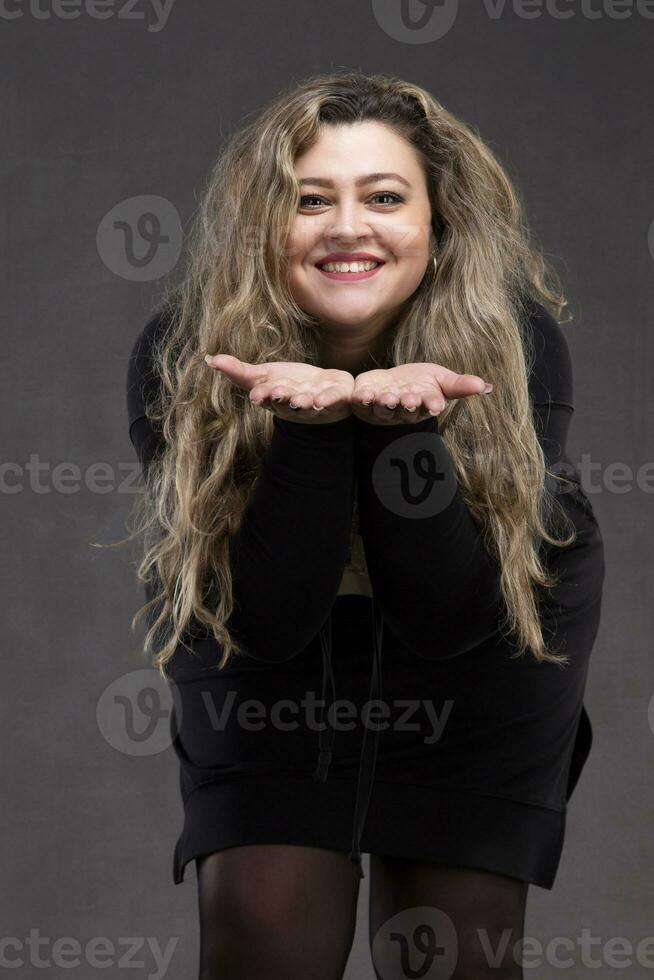 Beautiful fat woman with long curly hair and black dress blowing on her arms. photo