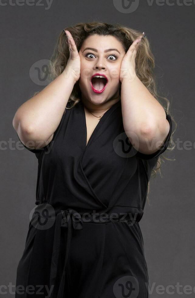 A beautiful fat woman with long curly hair screams loudly. A plump girl with an emotion of indignation and horror. photo