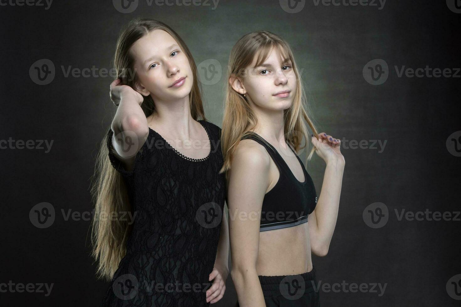 Two beautiful teenage girls on a dark background are looking at the camera. photo