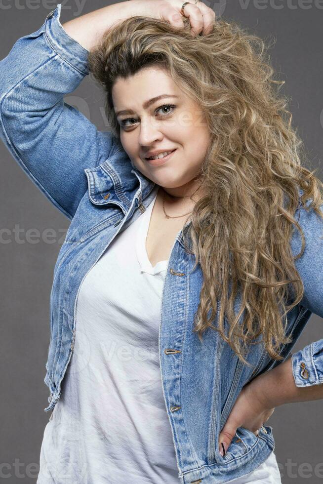 A beautiful plump girl in denim clothes looks at the camera and smiles. photo