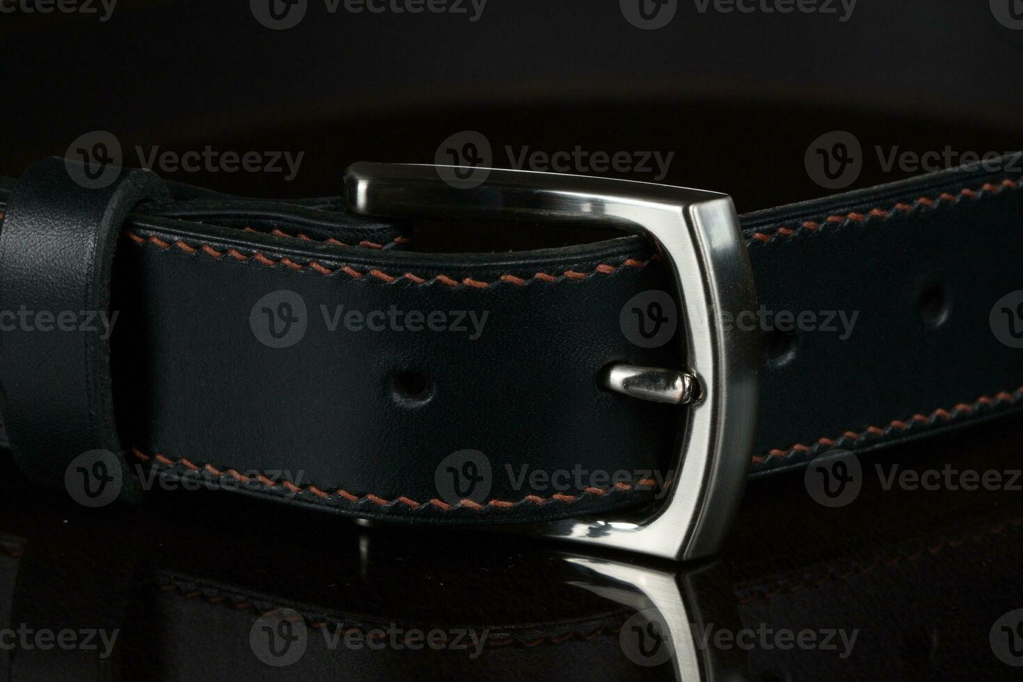 negro cuero cinturón con un metal hebilla en un oscuro antecedentes de cerca. foto