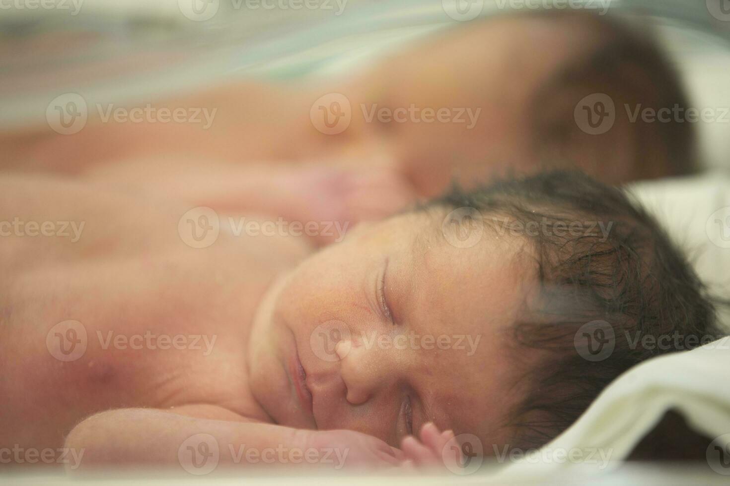 The face of a newborn baby behind the glass of a medical box. photo