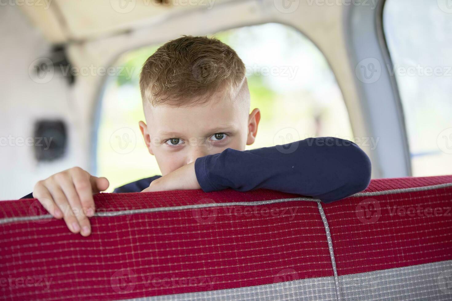 A handsome boy in the back seat of a car looks at the camera. photo